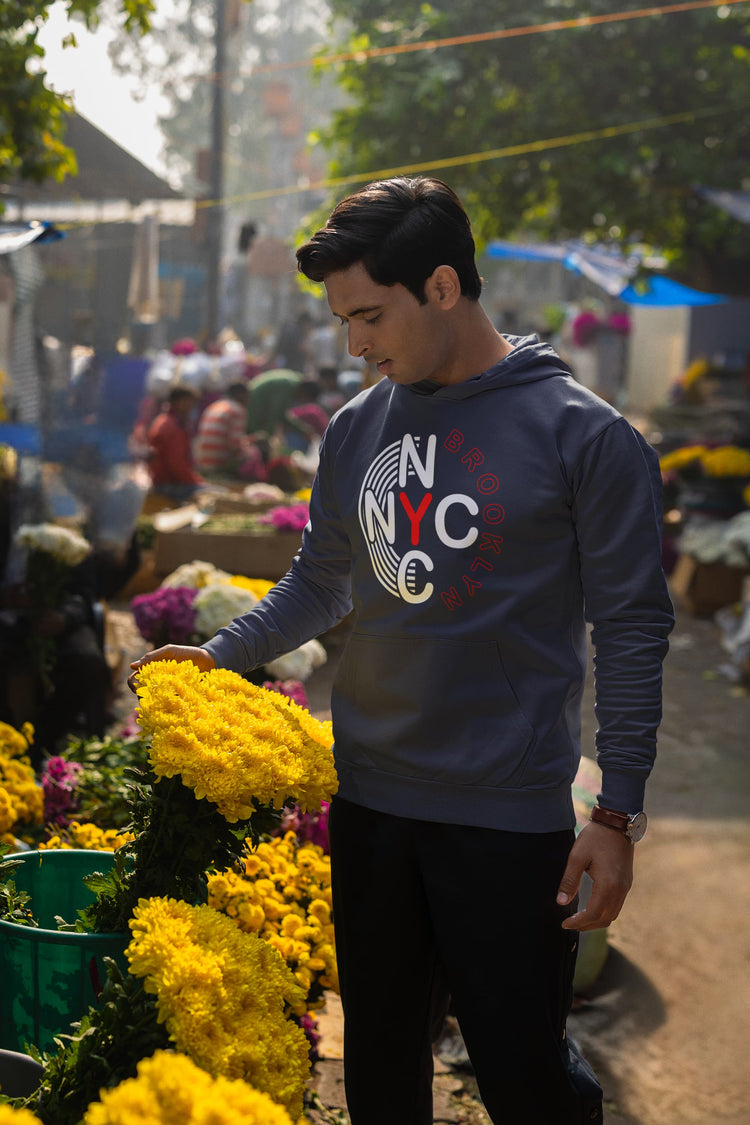 Man wearing a NYC sweatshirt among flowers and people at an outdoor market.