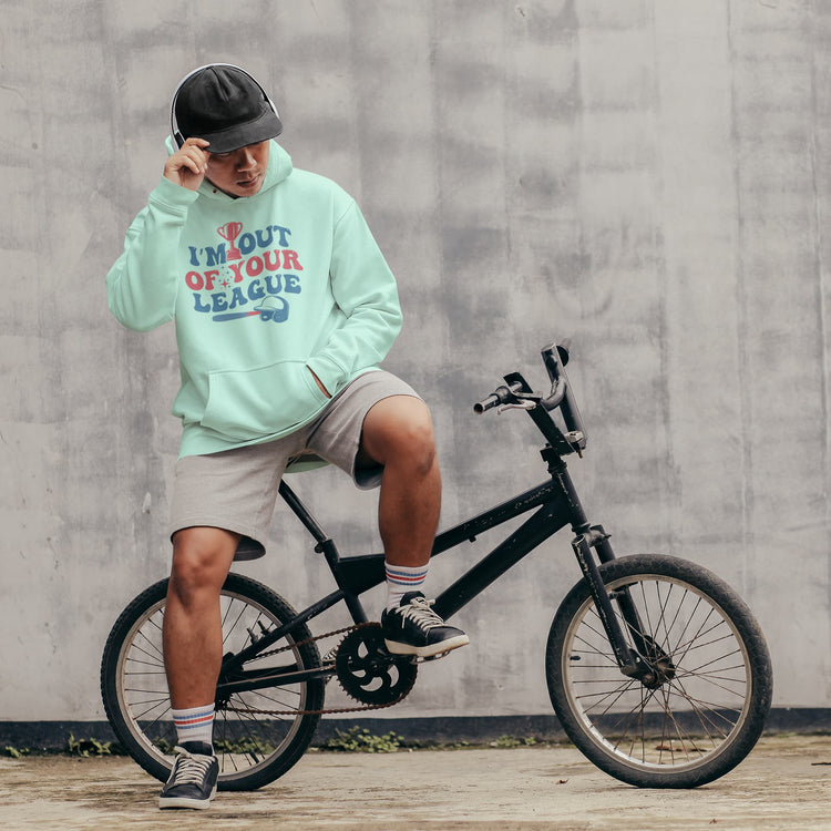Person wearing a light green hoodie with text, sitting on a black bicycle against a gray wall.