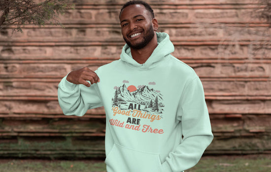 Man wearing a light green hoodie with nature-themed design and text, standing against a wooden wall.