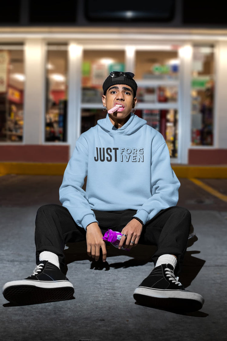 Person wearing a light blue hoodie with text, sitting on the ground in front of a store.