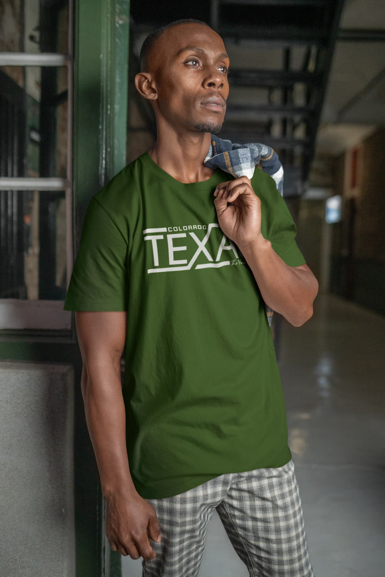 Man wearing a green t-shirt with text, holding a jacket, standing against a metallic wall.