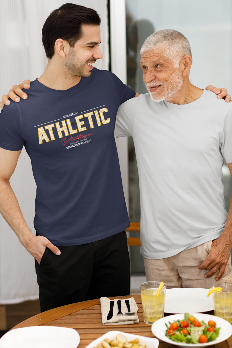 Two men standing together at a table with food and drinks, one wearing an &