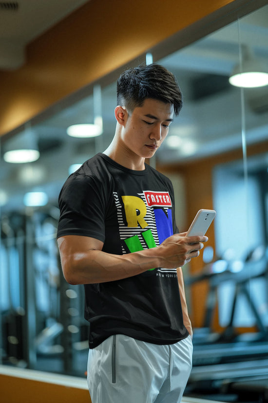Man in a gym wearing a black t-shirt with colorful graphics, looking at his phone.