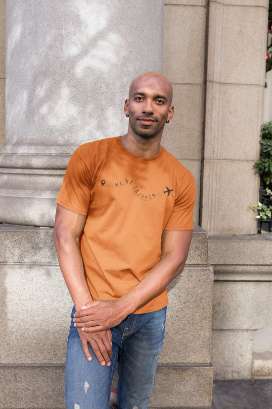 Man wearing an orange t-shirt with a logo, standing against a stone building.
