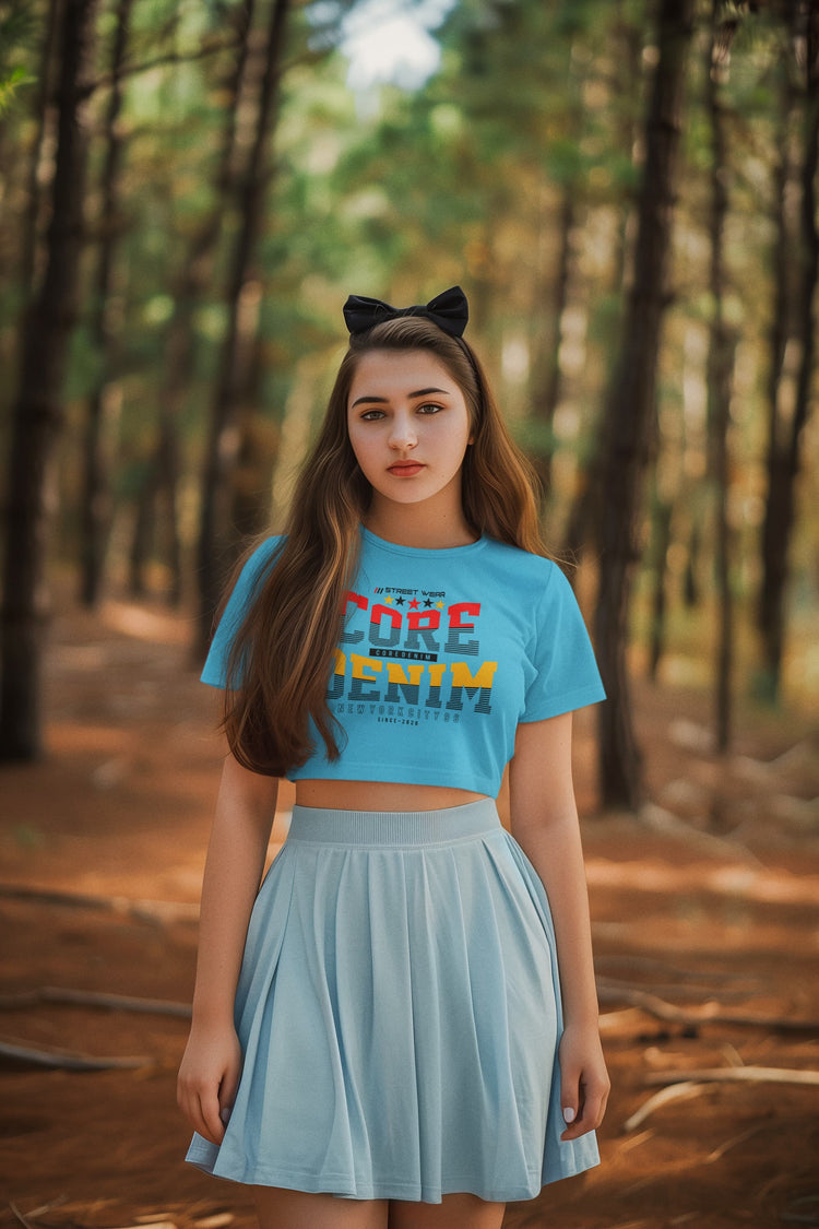 Woman wearing a blue t-shirt with text and a light blue skirt standing in a forest.
