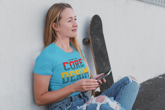Woman wearing a blue t-shirt with colorful text, holding a skateboard and a phone, against a light-colored wall.