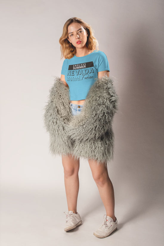 Woman wearing a blue t-shirt and gray fluffy coat against a plain background