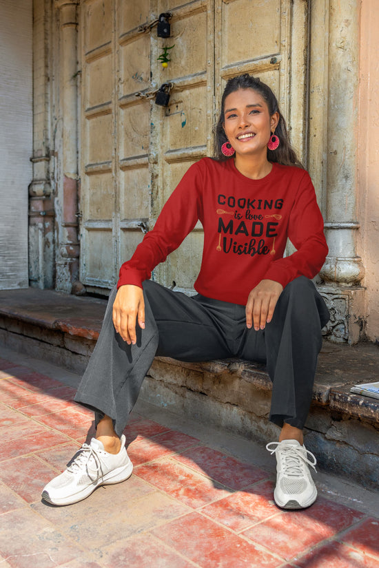 Woman wearing a red sweatshirt with text, sitting on steps in front of a rustic door.