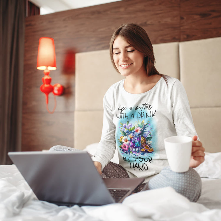 Woman sitting on a bed with a laptop and a mug, wearing a shirt with a floral design and text.