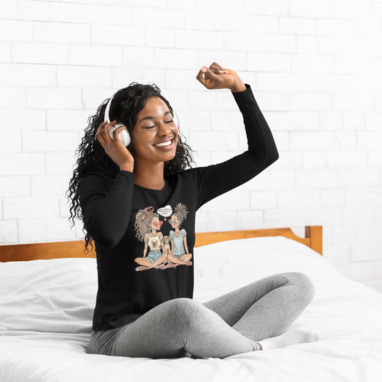 Woman wearing a black long-sleeve shirt with a graphic design, sitting on a bed.
