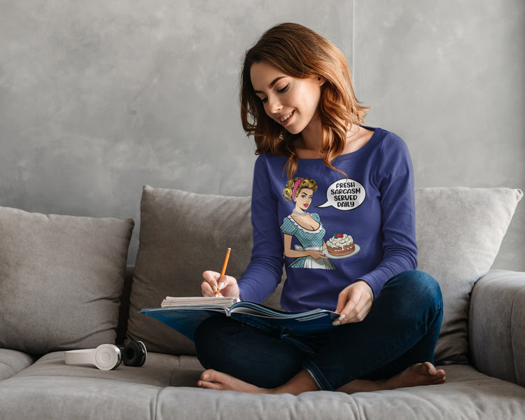 Woman sitting on a couch wearing a purple sweater with a graphic design, holding a notebook and pencil.