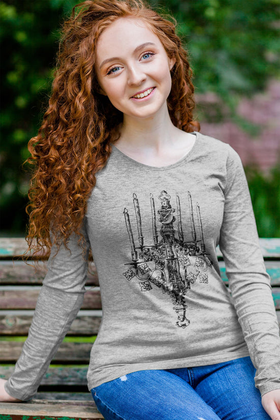 Person wearing a gray long-sleeve shirt with a graphic design, sitting on a bench outdoors.