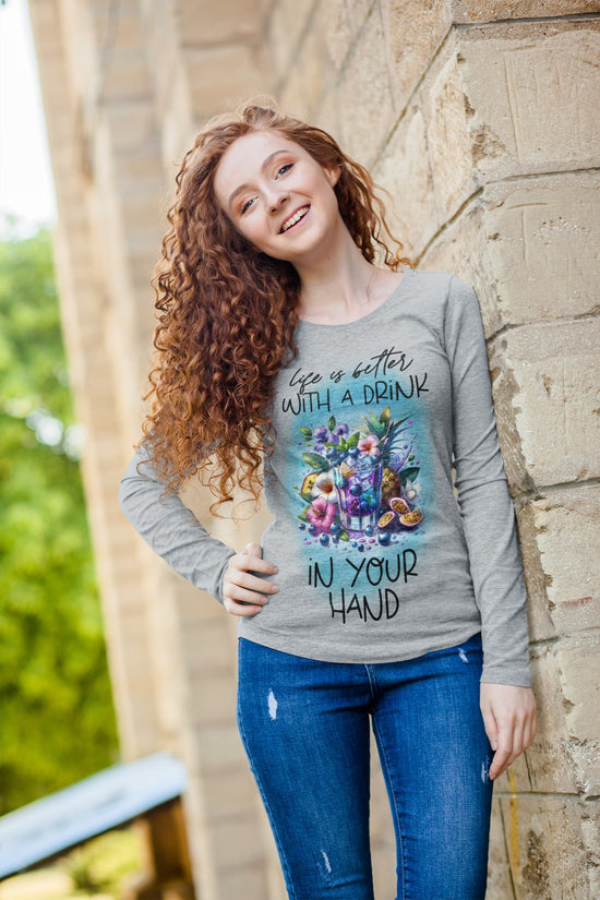 Young woman wearing a gray long-sleeve shirt with floral design and text, standing against a stone wall.
