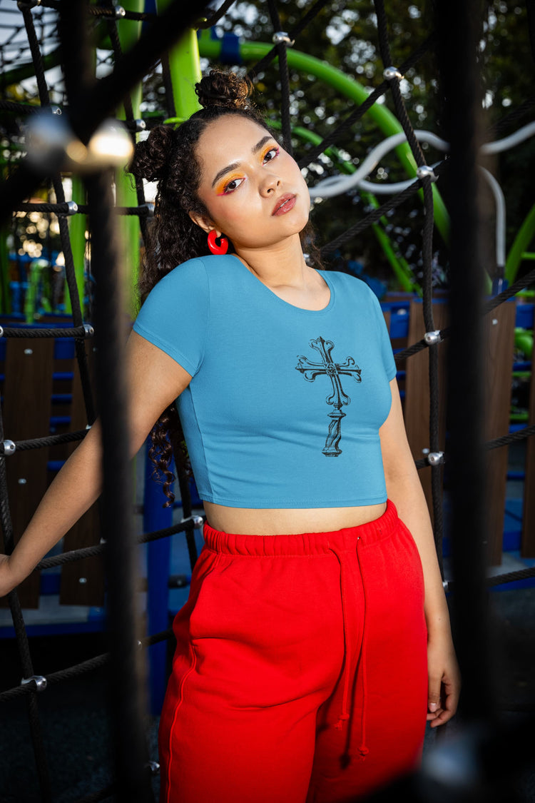 Woman wearing a blue crop top with a black graphic design and red pants standing in front of playground equipment.