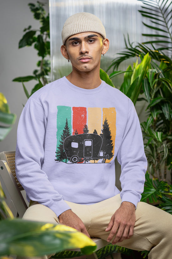 Person wearing a light blue sweatshirt with a camper design, sitting among plants.