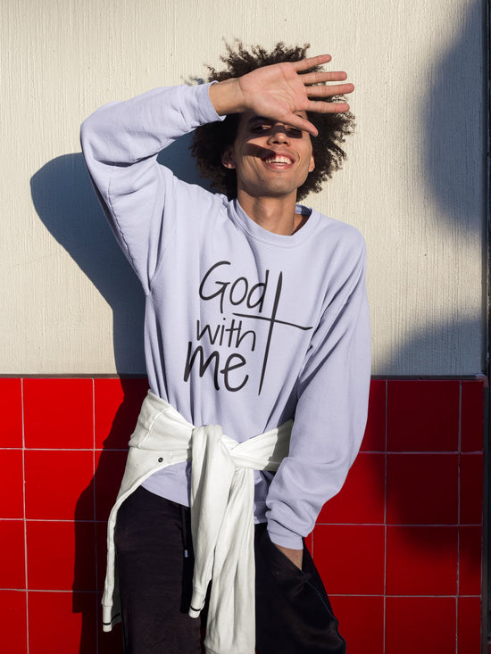 Person wearing a light purple sweatshirt with text, standing against a red and beige wall.