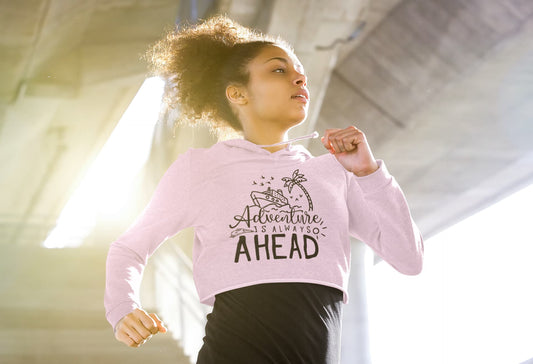 Woman wearing a pink sweatshirt with 'Adventure Awaits' text, standing indoors.