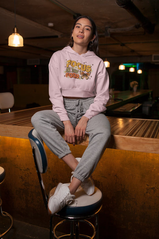Person wearing a pink hoodie with text, sitting on a bar stool in a dimly lit room.