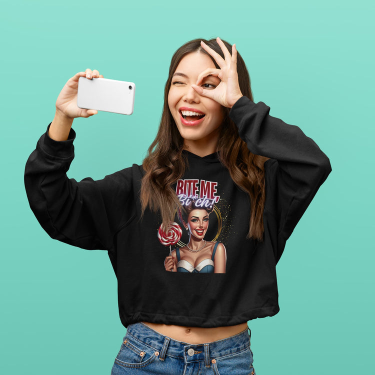 Woman wearing a black sweatshirt with graphic design, taking a selfie against a teal background
