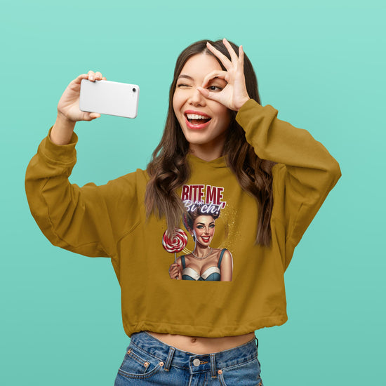 Woman wearing a mustard yellow sweatshirt with graphic design, taking a selfie against a teal background