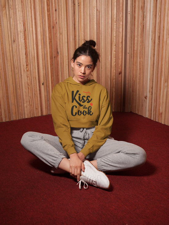 Person wearing a mustard yellow hoodie with text, sitting on the floor against a wooden paneled wall.