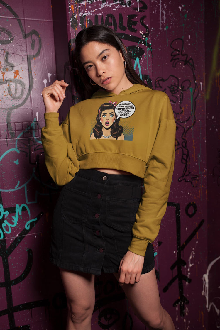 Woman wearing a mustard yellow sweatshirt with graphic design against a graffiti-covered wall.