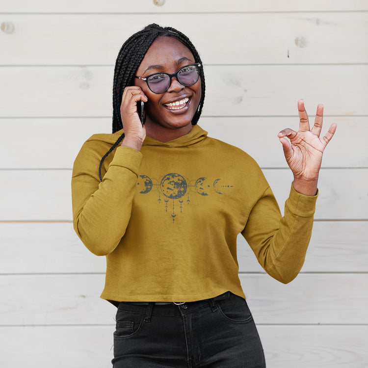 Woman wearing a mustard yellow hoodie with a graphic design, smiling and making a peace sign.