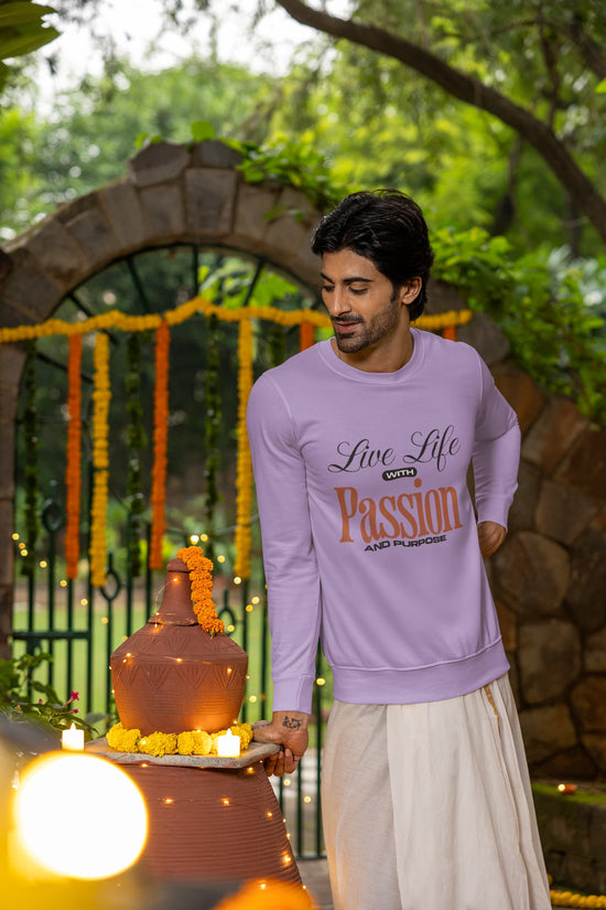 Man wearing a purple sweatshirt with text, standing outdoors with greenery and decorative archway in the background.