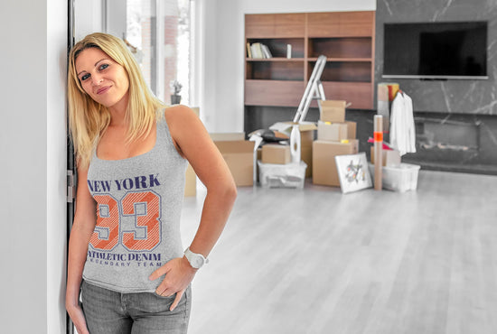 Woman wearing a tank top with text in a room with furniture and boxes.