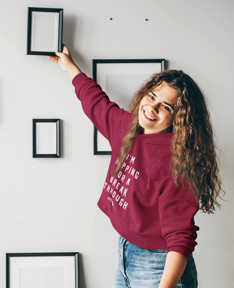 Person in a maroon sweatshirt with text, standing in a room with framed pictures on the wall.