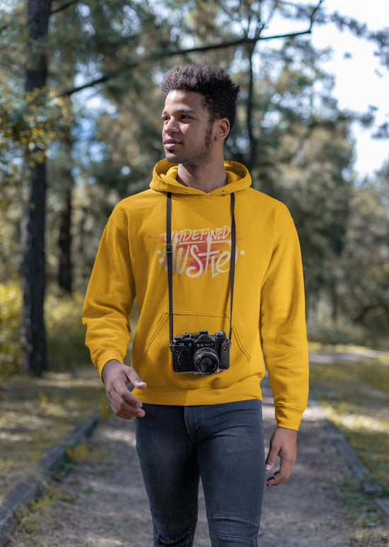 Man wearing a yellow hoodie with text and a camera design, standing outdoors.