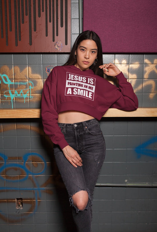 Person wearing a maroon sweatshirt with text, standing against a graffiti-covered wall.