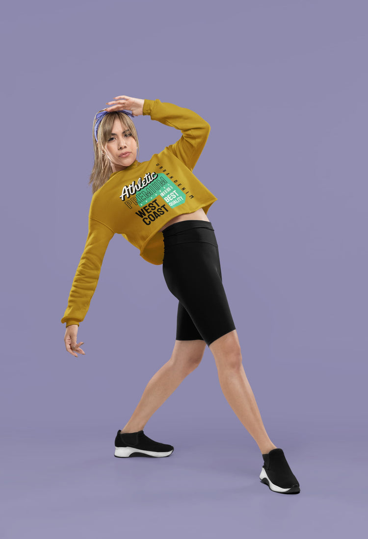 Woman wearing a yellow cropped sweatshirt with text, black shorts, and black sneakers on a purple background