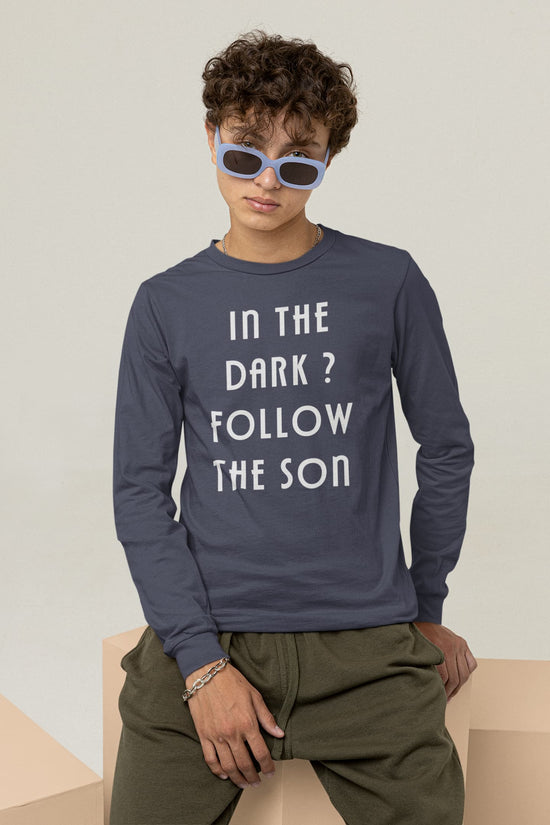 Person wearing a navy long-sleeve shirt with text and sunglasses, sitting on a beige surface.