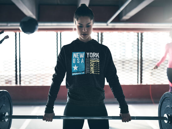 Person lifting a barbell in a gym wearing a hoodie with &