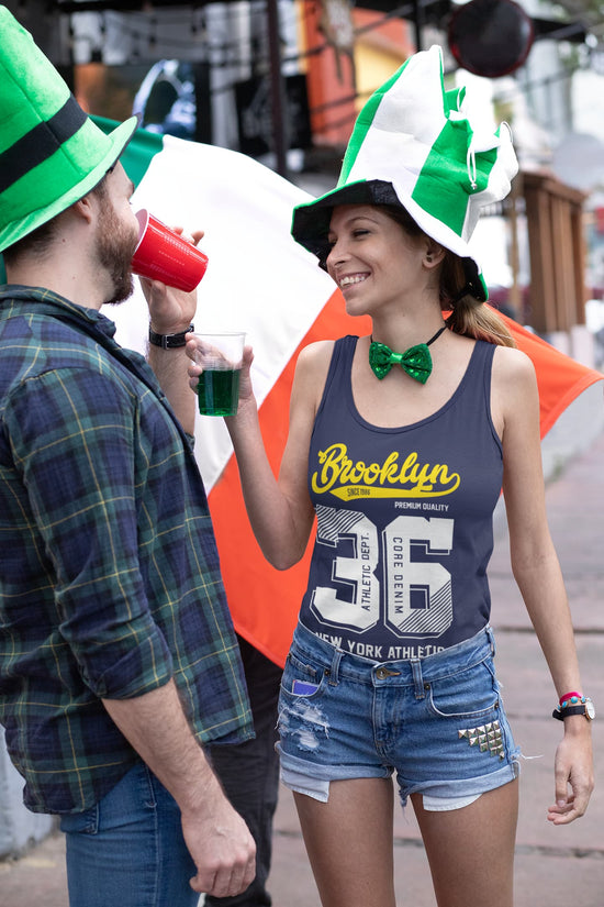 Two people wearing festive hats and drinking at a street event.