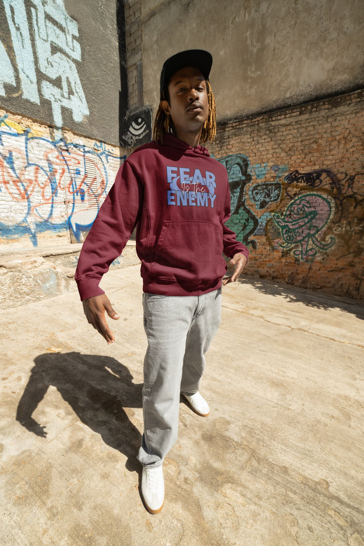 Person wearing a maroon hoodie with text, standing in front of graffiti-covered walls.