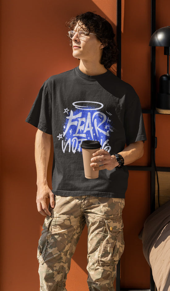Person wearing a black t-shirt with graphic design and holding a coffee cup against an orange wall.