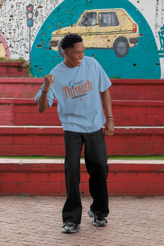 Person wearing a light blue t-shirt with text, standing in front of a colorful mural.
