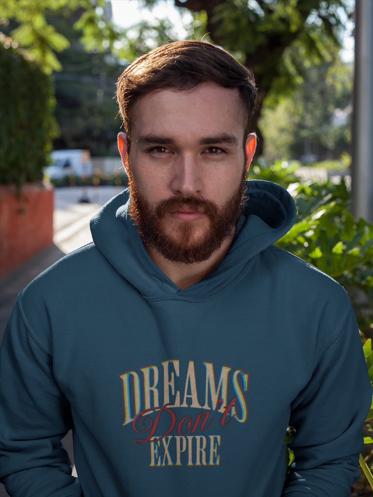 Man wearing a teal hoodie with 'Dreams Don't Expire' text outdoors.