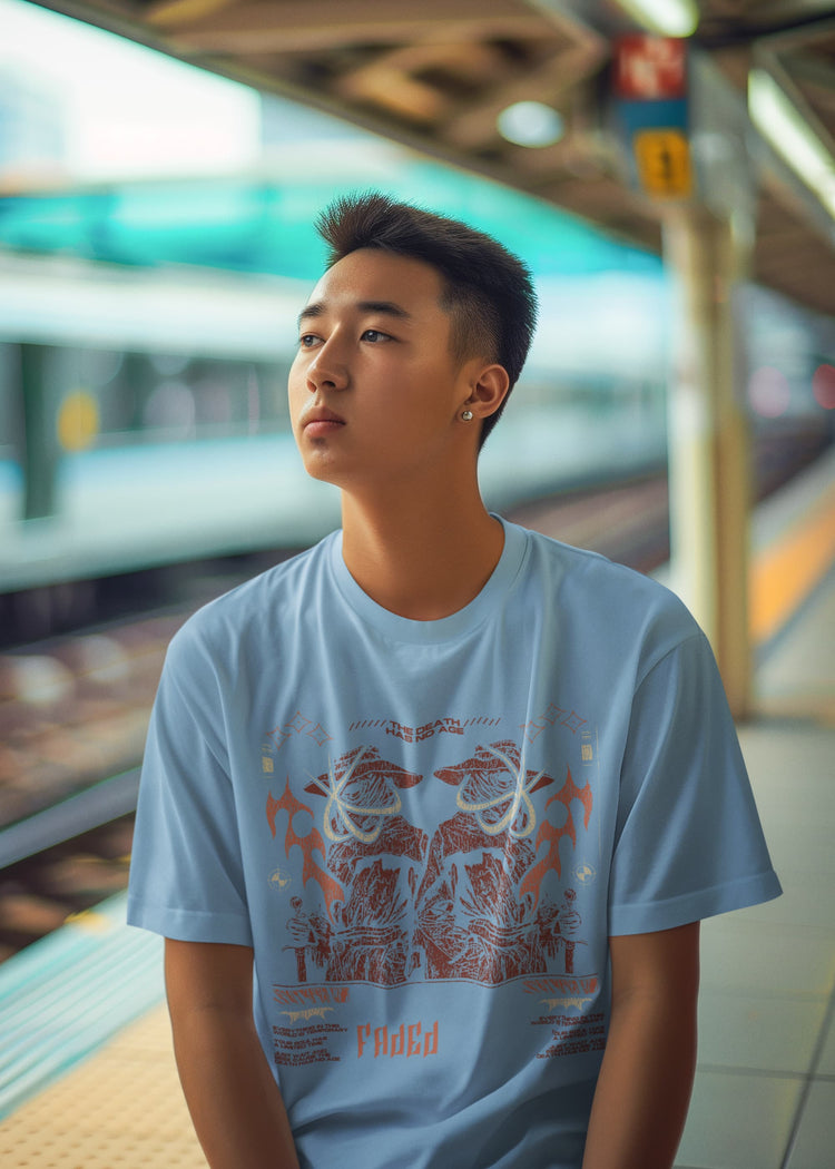 Person wearing a light blue t-shirt with a graphic design, standing in a train station.