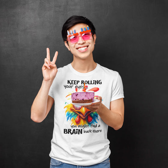 Person wearing a white t-shirt with a humorous design and text, holding a plate with a cake and making a peace sign.