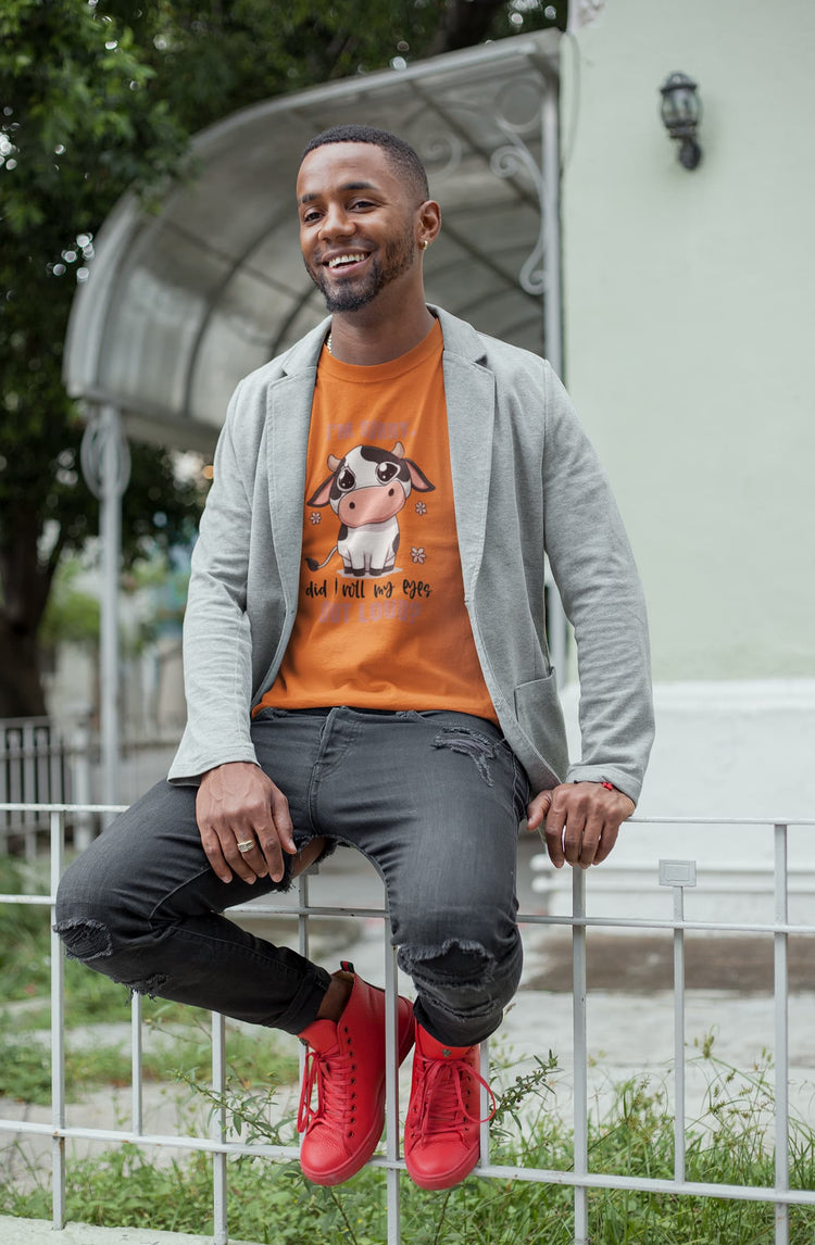 Man sitting on a bench wearing an orange t-shirt with a graphic design, gray cardigan, dark jeans, and red sneakers.