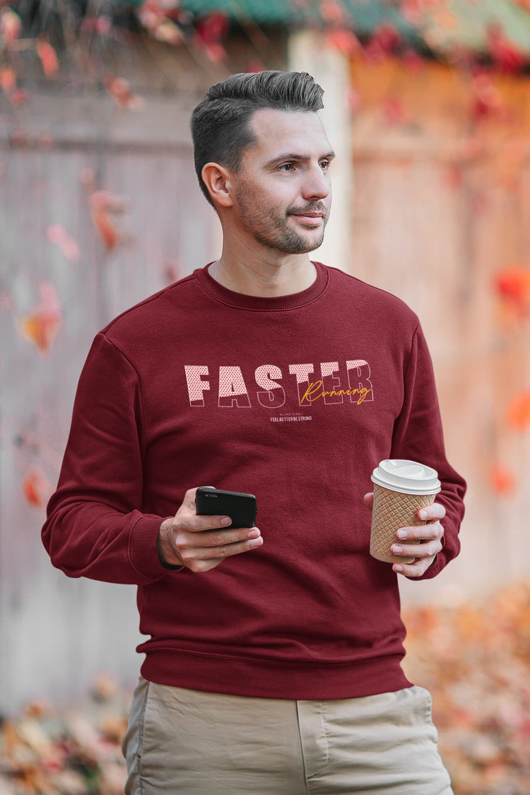 Man wearing a maroon sweatshirt with text, holding a phone and coffee cup, standing outdoors with autumn leaves.