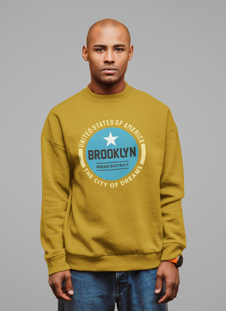 Man wearing a mustard yellow sweatshirt with a blue graphic design on a gray background