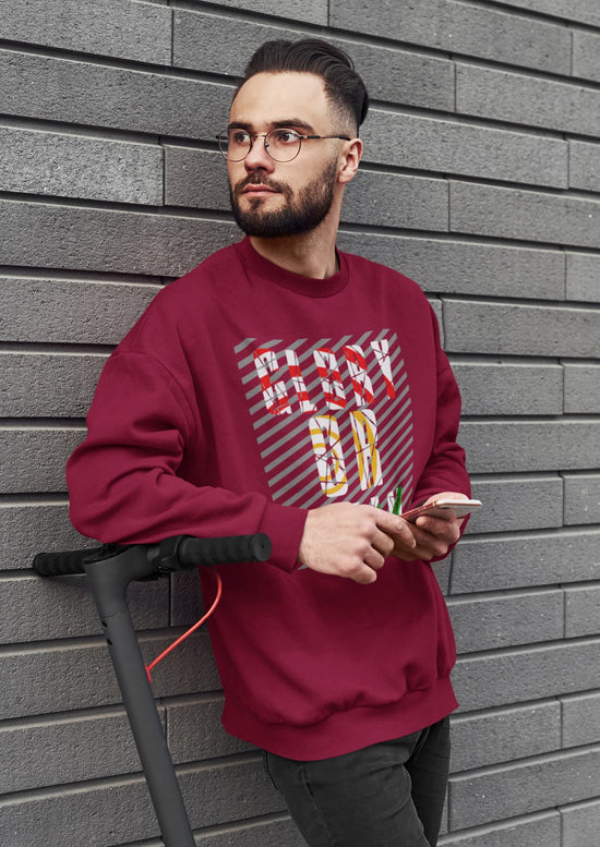 Man wearing a maroon sweatshirt with colorful text design, leaning against a gray brick wall.