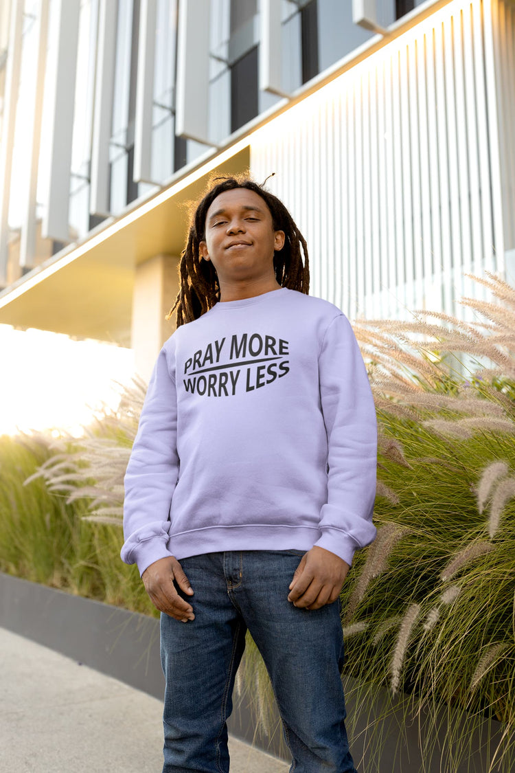 Person wearing a lavender sweatshirt with text, standing outdoors near plants and a building.