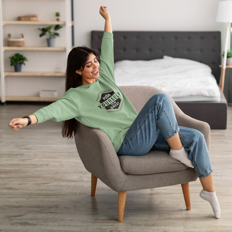 Woman sitting in a chair wearing a green sweatshirt and blue jeans in a bedroom.