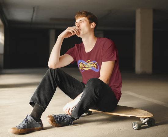 Person sitting on a skateboard wearing a maroon t-shirt with a logo in an indoor setting
