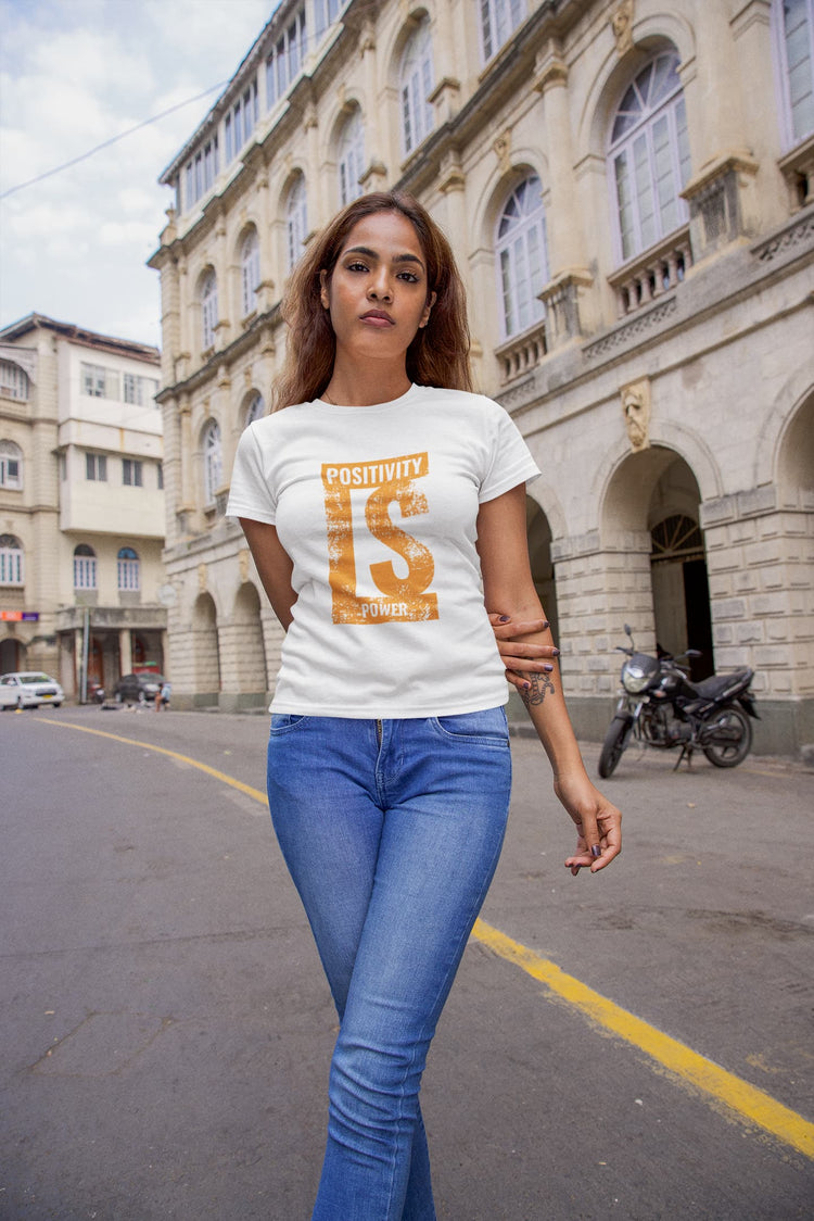 Woman wearing a white t-shirt with text and blue jeans standing on a street with buildings in the background